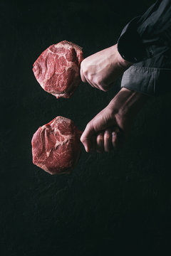 Man's hands holding raw uncooked black angus beef tomahawk steaks on bones over dark background. Rustic style. Toned image