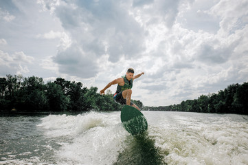 Young and athletic man wakesurfing on the board