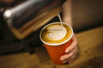 Barista drawing latte art in a orange cup