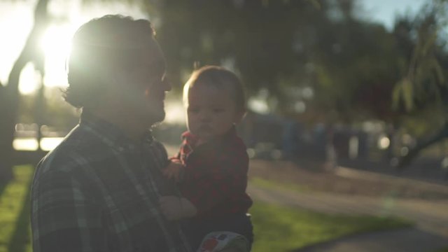 Young dad hugs and kisses his baby son in the park at sunset