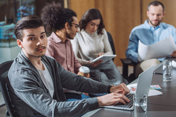 young successful businessman working with laptop at office with blurred colleagues on background