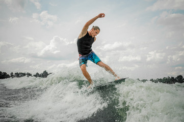 Handsome athletic man wakesurfing on the board against the sky