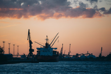 Fototapeta na wymiar Silhouette on cargo ships and cranes in industrial harbor in sunset