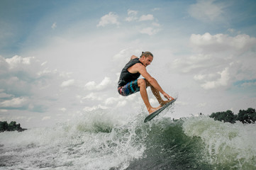 Young guy wakesurfing on the board down the river