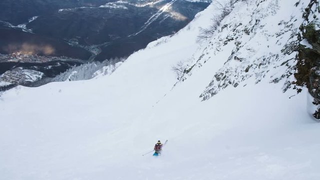 A skier in a bright suit goes down from a steep mountain, freeride in the mountains, slow motion.