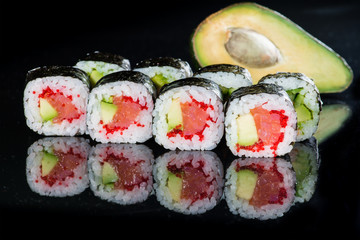 Tasty fresh Sake Avocado Maki sushi with rice, avocado, tobiko and salmon on dark background