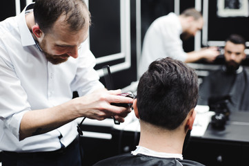 Obraz premium Master cuts hair and beard of men in the barbershop, hairdresser makes hairstyle for a young man