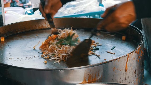 Seller of street food fries traditional thai rice noodles with eggs, chicken and sprouts. Asian street food