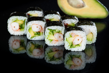 Japanese cuisine. Appetizing maki sushi rolls with rice, avocado, cucumber and shrimp on dark background
