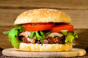 Delicious tasty burger with beef, tomatoes, salad and sauce on board on wooden  background, close-up
