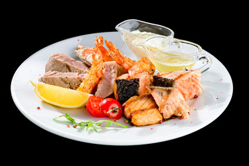 Appetizing Tuna steak with tomato, lemon and sauce in a white plate isolated on black background, close-up