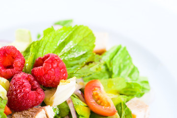 Appetizing fresh vegetarian salad with different berries, tomatoes, meat, basil leaves and sauce, close-up. For menu design