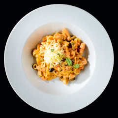 Traditional Italian cuisine. Appetizing tagliatelle pasta with seafood, cheese and basil in a white plate isolated on dark background. Top view, flat lay