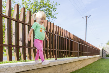 A little girl steals from the edge of a fence.