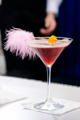 Alcoholic pink cocktail in a martini glass with straw, shallow dof
