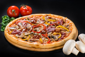 Delicious pizza with salami, beef, mozzarella, pepper and sauce on wooden board on dark background