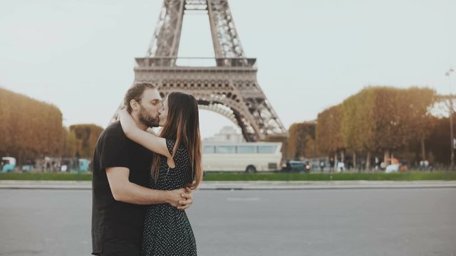 Young happy couple walking near the Eiffel tower in Paris, France. Man and woman hugging and kissing on the street.