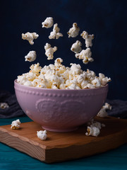 Popcorn in pink bowl on wooden board on dark green background. Popcorn falling down in bowl. Food in motion