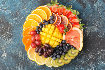 Healthy fruits and berries platter in rainbow colours, strawberries, mango, grapes, oranges, kiwis, lemons on the blue table, copy space for text, selective focus