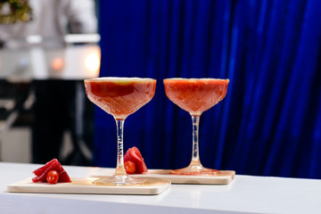Two martini glasses with red alcoholic cocktail on the wooden board on blue background