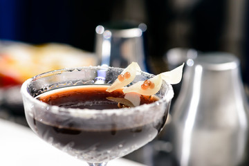 Martini glass with dark alcoholic cocktail at the bar counter on blue background, close-up