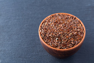 Close-up picture of flax seeds in a clay bowl isolated on dark background.