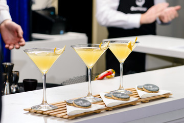 Line of three martini glasses with yellow cocktail on bar counter, selective focus