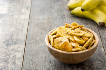 Banana chips in wooden bowl on wooden table background