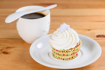 Appetizing sweet dessert. White glaze cupcake with cream and cup of coffee on the wooden table