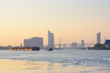 Tugboat take barges downstream on the river to the sea under the sunset in the city.