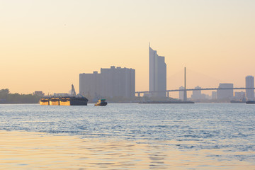 Obraz premium Tugboat take barges downstream on the river to the sea under the sunset in the city.