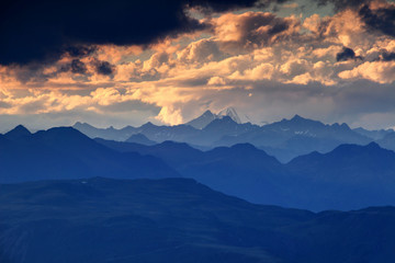 Jagged blue ridge silhouettes, snowcapped Rotspitze Pizzo Rosso peak and fluffy orange clouds at sunset, Venediger Group and Villgraten Mountains Defereggen Alps Hohe Tauern Osttirol Austria Europe