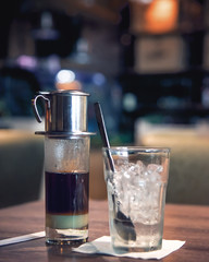 Traditional vietnamese coffee with condensed milk and glass of ice cube in moody dim cafe restaurant background - obrazy, fototapety, plakaty