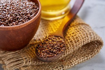 Flax seeds in bowl and flaxseed oil in glass bottle on light textured background, top view, close-up, selective focus