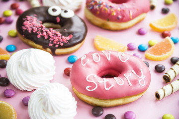 Junk food. Donuts, marmalade, chocolate sticks and balls, and meringues are scattered on a pink background. Unhealthy food concept