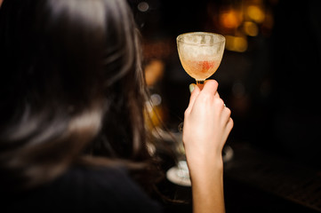 Back view of brunette woman holding a glass with cocktail