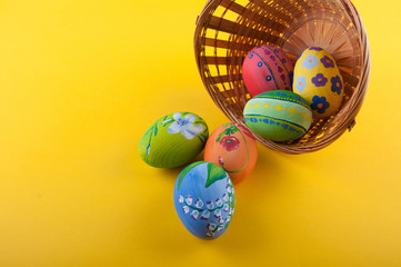 Several Easter eggs laying in basket and near on yellow background