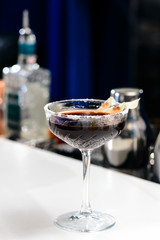 Black alcoholic cocktail in martini glass on blue background, shallow dof