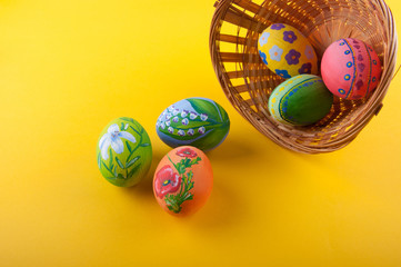 Variety of painted Easter eggs laying on yellow background near withy basket