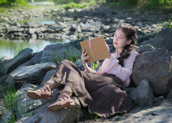 Young woman in a Boho style is reading book on the river bank.