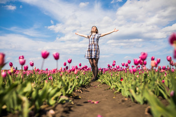 beautiful happy woman in a field of pink tulips on blue sky on background