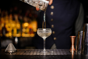 Bartender pouring a ready alcoholic cocktail into the glass