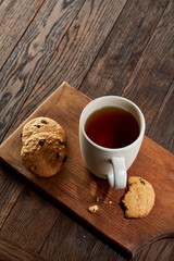 Cup of tea with cookies on a wooden cutting board on vintage background, top view