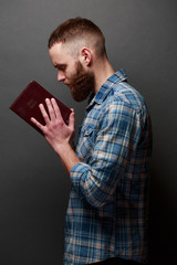 Handsone man reading and praying over Bible in a dark room over gray texture