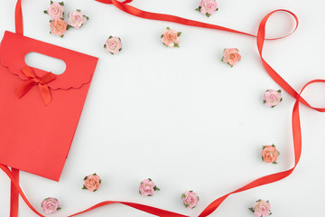 Red gift bag with pink and orange paper flowers with red ribbon on white background with copy space