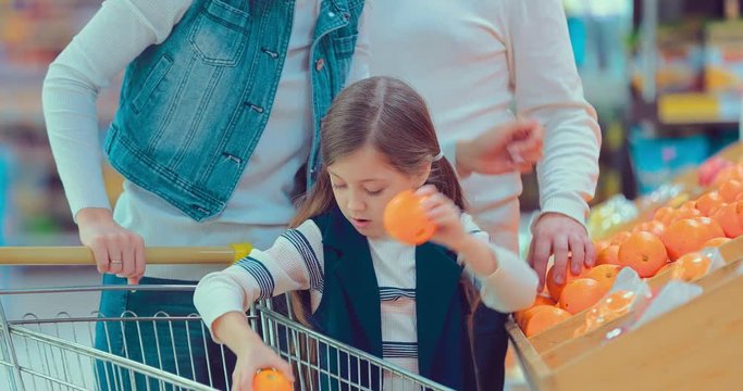 Little girl is buying oranges. Girl herself chooses food in the hypermarket