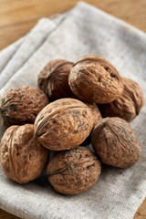 A stack of hard shells of walnuts piled together on light grey fabric cotton tablecloth, selective focus