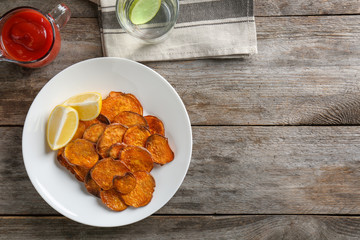 Plate with tasty sweet potato chips on wooden table, top view