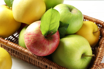 Juicy apples in basket on wooden table, closeup