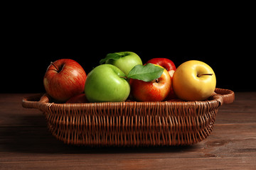 Juicy apples in basket on table against dark background